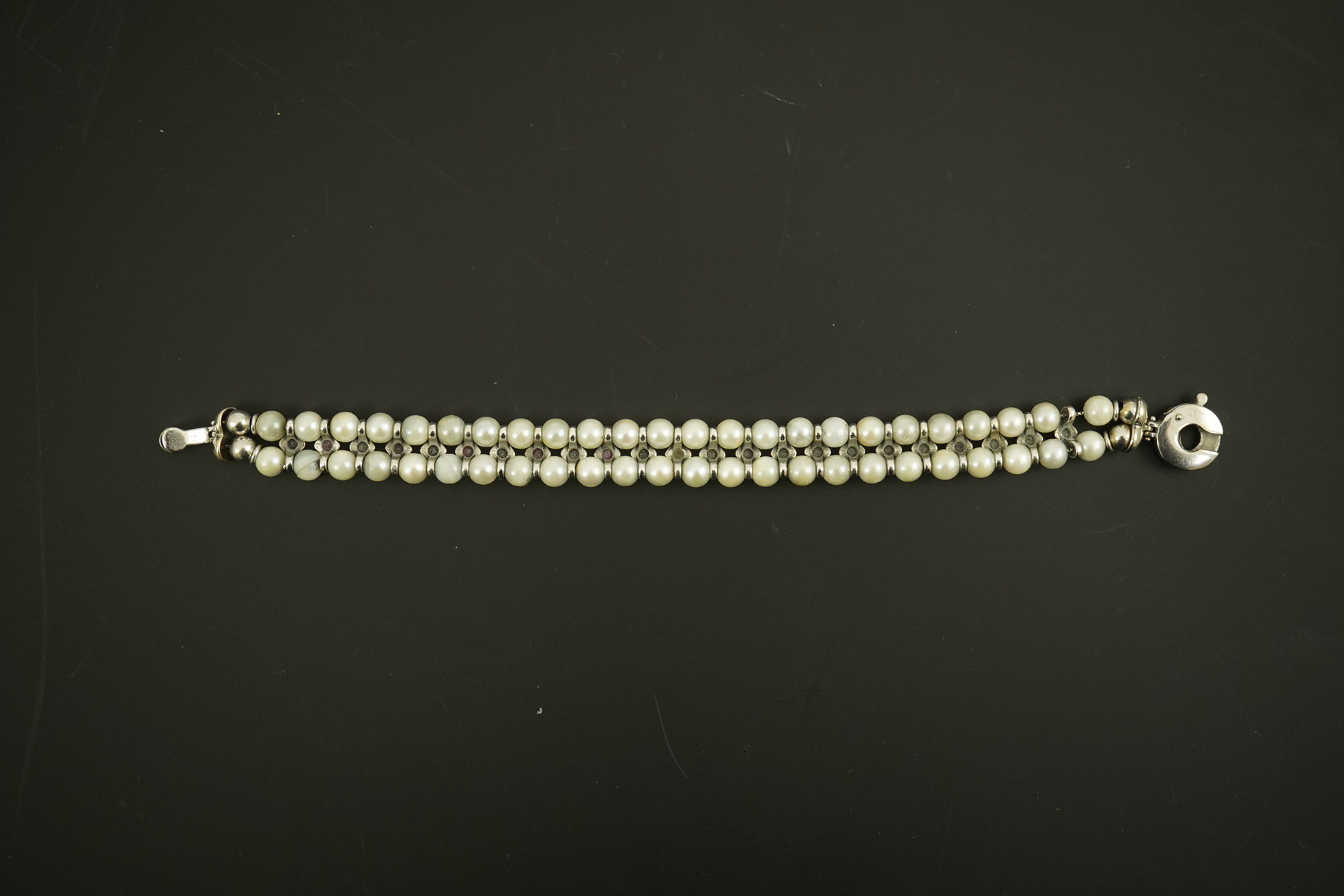 A late 20th century 18k white gold and two row cultured pearl bracelet, set with single row of cabochon rubies and sapphires